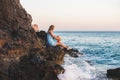 Young blond woman tourist in blue dress relaxing on stone rocks by the wavy sea at sunset. Alanya, Mediterranean region Royalty Free Stock Photo