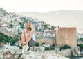 Young blond woman tourist relaxing on ancient fortress wall of Alanya castle. Kizil Kule or Red Tower at background. Royalty Free Stock Photo