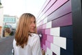 Young blond woman walking down an looking over her shoulder while next to mural painted in geometric shapes in shades of purple