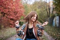 Young blond woman, wearing colorful cardigan, sitting on ground, playing with her hair in countryside with red green and yellow Royalty Free Stock Photo