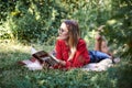 Young blond woman, wearing eyeglasses red blouse and black skirt, lying on the green grass in the park, holding open book, Royalty Free Stock Photo