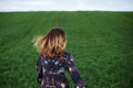 Young blond woman, wearing long dark boho dress, holding black hat running away in green field in spring. Model posing outside in Royalty Free Stock Photo