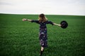 Young blond woman, wearing long dark boho dress, holding black hat running away in green field in spring. Model posing outside in Royalty Free Stock Photo