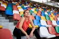 Young blond woman, wearing orange top, black leggings, orange sneakers, sitting on the stairs on stadium tribune, relaxing after