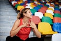 Young blond woman, wearing orange top, black leggings, orange sneakers, sitting on the stairs on stadium tribune, relaxing after