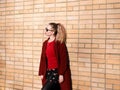 Young blond woman wearing sunglasses, woolen coat is standing by the brick wall Royalty Free Stock Photo