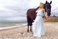 Young blond woman wears elegant dress, posing with black horse Royalty Free Stock Photo