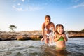 Young blond woman in white bikini and small happy girl having fun in sea water with rocky beach at background Royalty Free Stock Photo