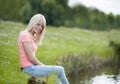 Young blond woman in white seated at the lake