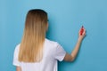 Young Woman Is Writing On A Blue Wall, Rear View