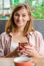 Young blond woman is working on her smartphone. Red cup of red tea stand on a table in cafe.