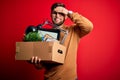 Young blond worker man with beard and blue eyes fired holding cardboard box stressed with hand on head, shocked with shame and Royalty Free Stock Photo