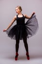 Young blonde ballerina girl dance and posing in black tutu and ballet shoes on grey background. Royalty Free Stock Photo