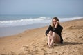 Young, blonde, beautiful woman in a bikini and black colored shirt sitting on the beach, sad, lonely, sorry, depressed. Concept Royalty Free Stock Photo
