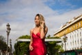 Young, blonde, beautiful woman in a red dress is visiting seville. The woman poses for the camera very elegant and like a model.