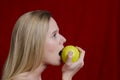 Young blonde biting on apple on red background Royalty Free Stock Photo