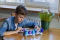 Young blonde boy Drawing Easter Eggs at Home. Easter Holiday at Home. Blue Easter Eggs.