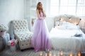 A young blonde bride in a magnificent purple dress is in the bedroom. In the room candles and bouquets of flowers.