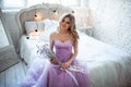 A young blonde bride in a magnificent purple dress sitting on the bed. In the room candles. Girl holds in the hands of