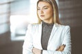 Young blonde business woman or female student standing straight and posing at camera in sunny office Royalty Free Stock Photo