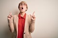 Young blonde business woman with short hair wearing glasses and elegant jacket amazed and surprised looking up and pointing with Royalty Free Stock Photo