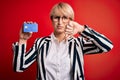 Young blonde business woman with short hair wearing glasses holding credit card with angry face, negative sign showing dislike Royalty Free Stock Photo