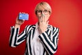Young blonde business woman with short hair wearing glasses holding credit card cover mouth with hand shocked with shame for Royalty Free Stock Photo