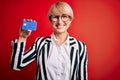 Young blonde business woman with short hair wearing glasses holding credit card with a happy face standing and smiling with a Royalty Free Stock Photo