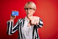 Young blonde business woman with short hair wearing glasses holding credit card pointing with finger to the camera and to you, Royalty Free Stock Photo
