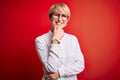 Young blonde business woman with short hair wearing glasses over red background looking confident at the camera smiling with Royalty Free Stock Photo