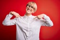 Young blonde business woman with short hair wearing glasses over red background looking confident with smile on face, pointing Royalty Free Stock Photo