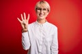 Young blonde business woman with short hair wearing glasses over red background showing and pointing up with fingers number four Royalty Free Stock Photo