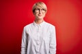 Young blonde business woman with short hair wearing glasses over red background smiling looking to the side and staring away Royalty Free Stock Photo