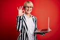 Young blonde business woman with short hair wearing glasses working using computer laptop doing ok sign with fingers, excellent Royalty Free Stock Photo