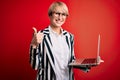 Young blonde business woman with short hair wearing glasses working using computer laptop happy with big smile doing ok sign, Royalty Free Stock Photo