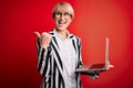 Young blonde business woman with short hair wearing glasses working using computer laptop pointing and showing with thumb up to Royalty Free Stock Photo