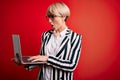 Young blonde business woman with short hair wearing glasses working using computer laptop scared in shock with a surprise face, Royalty Free Stock Photo