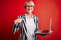 Young blonde business woman with short hair wearing glasses working using computer laptop with surprise face pointing finger to Royalty Free Stock Photo