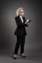 Young blonde business woman stands in a male suit in eyeglasses holding a black folder ane writes with a pen Royalty Free Stock Photo