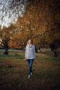 Young blonde Caucasian woman walking straight ahead looking at camera smiling wearing grey sweater, blue jeans and Royalty Free Stock Photo