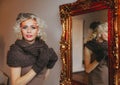 Young blonde curly woman with make-up looking in camera and standing near the big mirror Royalty Free Stock Photo