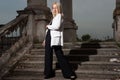 A young blonde eighteen, generation Y, in a white jacket and black pants, standing on the steps of a vintage building. Fashion Royalty Free Stock Photo