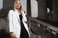 A young blonde eighteen, generation Y, in a white jacket and black pants, standing on the steps of a vintage building. Fashion Royalty Free Stock Photo