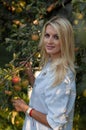 Vertical closeup portrait of a beautiful blonde on a background of an apple tree full of ripe apples Royalty Free Stock Photo