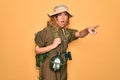 Young blonde explorer woman with blue eyes hiking wearing backpack and water canteen Pointing with finger surprised ahead, open