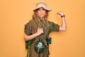 Young blonde explorer woman with blue eyes hiking wearing backpack and water canteen Strong person showing arm muscle, confident Royalty Free Stock Photo