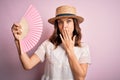 Young blonde fashion girl using wooden spanish hand fan on a hot summer day cover mouth with hand shocked with shame for mistake,