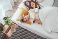 Young blonde female dressed pijama lying in the cozy bed under the blanket and browsing a smartphone internet. Sweet cozy home and Royalty Free Stock Photo