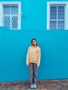 Young blonde female wearing a yellow hoodie in front of a blue building in Bo-Kaap district