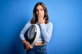 Young blonde fitness girl holding scale dieting for heatlhy weight over blue background cover mouth with hand shocked with shame